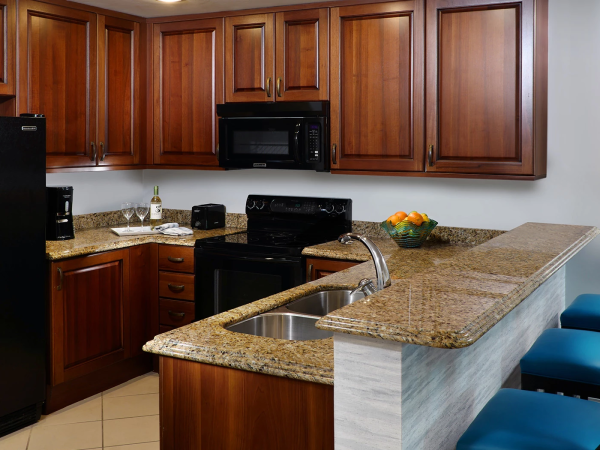 Kitchen with wooden cabinets, black appliances, granite countertops, island bar, and blue bar stools; bright and clean.