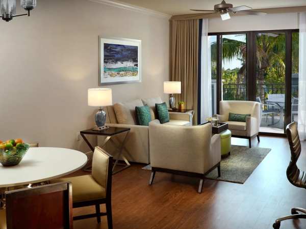 A stylish living room and dining area with beige sofas, green accents, wood floors, and a balcony view; chic modern decor, sunny lighting.