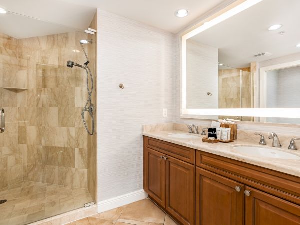 A modern bathroom with a glass-enclosed walk-in shower and a double-sink vanity with a large backlit mirror.