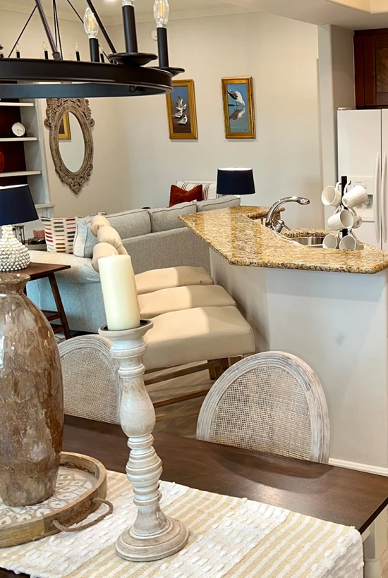 A modern, open-concept kitchen and dining area with granite countertops, wooden cabinets, a breakfast bar, and a cozy living space nearby.