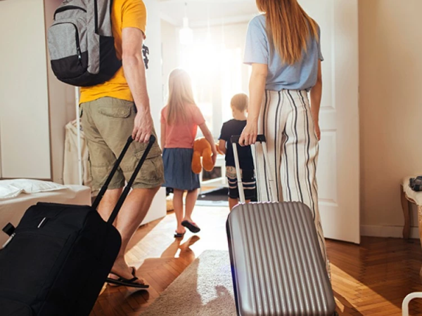 A family travels home with kids and suitcases, entering a bright hallway as a woman and man lead the way, packing bags for a trip.