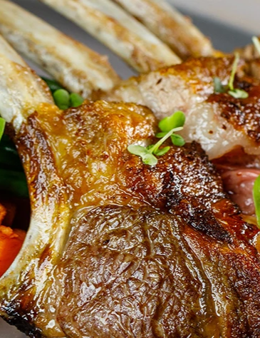 A grilled lamb rack served with roasted vegetables (sweet potato, greens, pecans), small herbs, and a crisp crusty finish, plated beautifully.