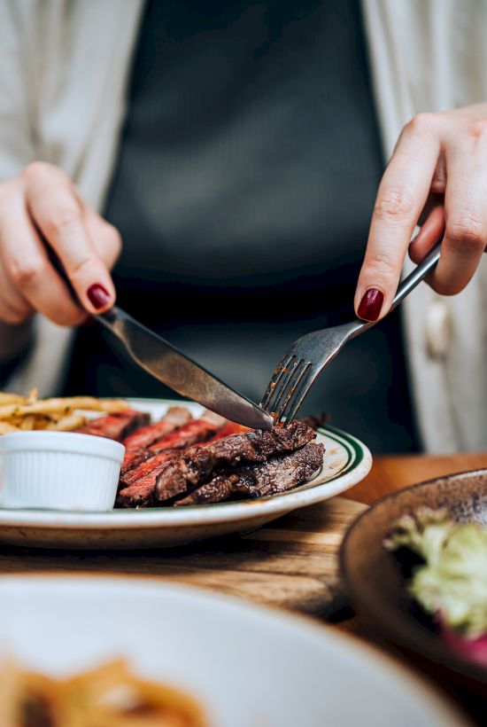 A diner cuts a steak with a fork and knife at a restaurant table.