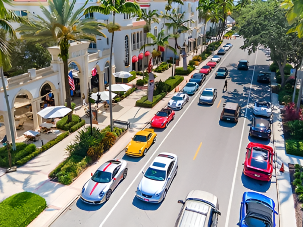 Colorful coastal street with palm trees, luxury shops, and a line of parked sports cars along a sunny avenue. End.