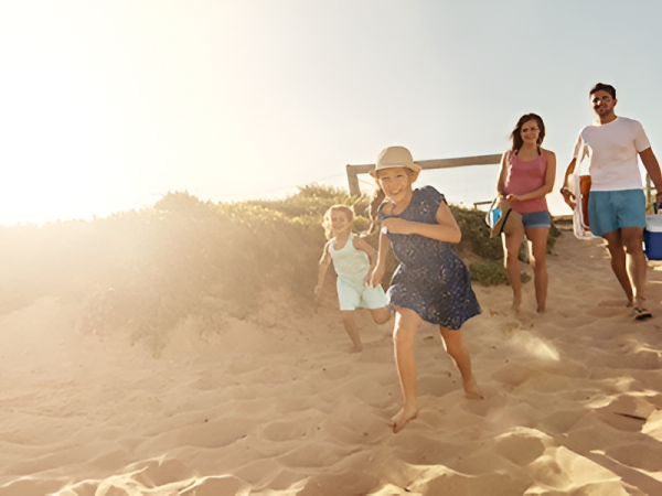 A family runs down a sunny beach on the sand, carrying a cooler and enjoying a day out together.