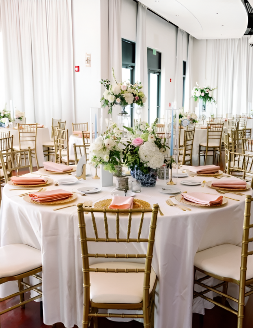 A stylish event setup with round tables, gold chairs, and elegant floral centerpieces in a bright, modern venue.