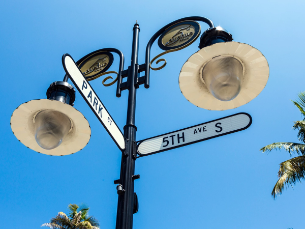A stylish street sign post with lanterns, palm trees, and bright blue sky, marking Park and 5th Ave South&mdash;vivid coastal vibes.