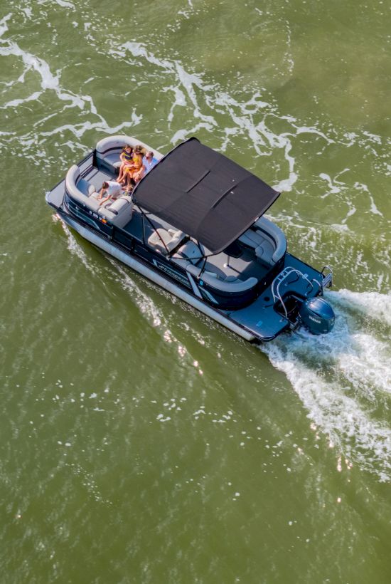 A small motorboat with a black canopy cruises through greenish water, leaving white wake as passengers enjoy the ride.