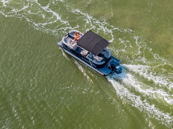 A blue motorboat with a black canopy speeds through greenish water, leaving white wake trails behind as passengers enjoy the ride.