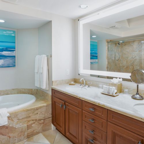 A luxurious bathroom with a built-in tub, double sink vanity, marble countertops, and a large mirror, plus calming blue wall art.
