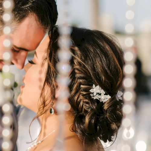 A close-up of a couple kissing at a wedding, softly framed by hanging beads and a decorative hairpiece on the bride.