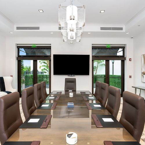 A sleek conference room with a long table, brown leather chairs, a wall-mounted TV, glass doors, lush greenery outside, and modern decor. ending with period.