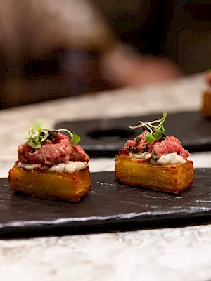 Small bite-sized hors d'oeuvres: toasted bread with toppings, dollops of meat or spread, and microgreens, elegant and plated on slate.