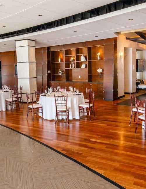 A banquet hall setup with round tables, white tablecloths, and wooden chairs, ready for a formal event.