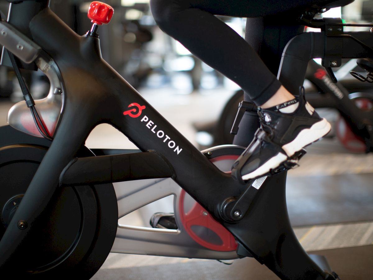 A Peloton bike in a studio, with a rider&rsquo;s legs and handlebars visible in the frame.