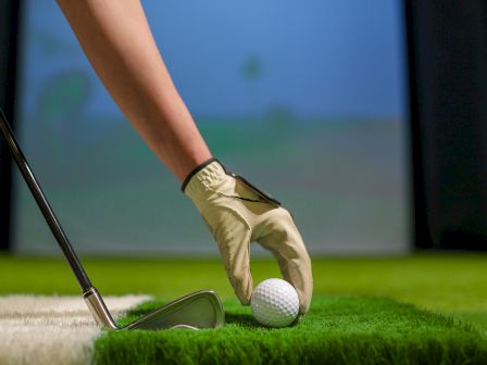 A golfer&rsquo;s gloved hand swings a club as a ball rests on the green during play.