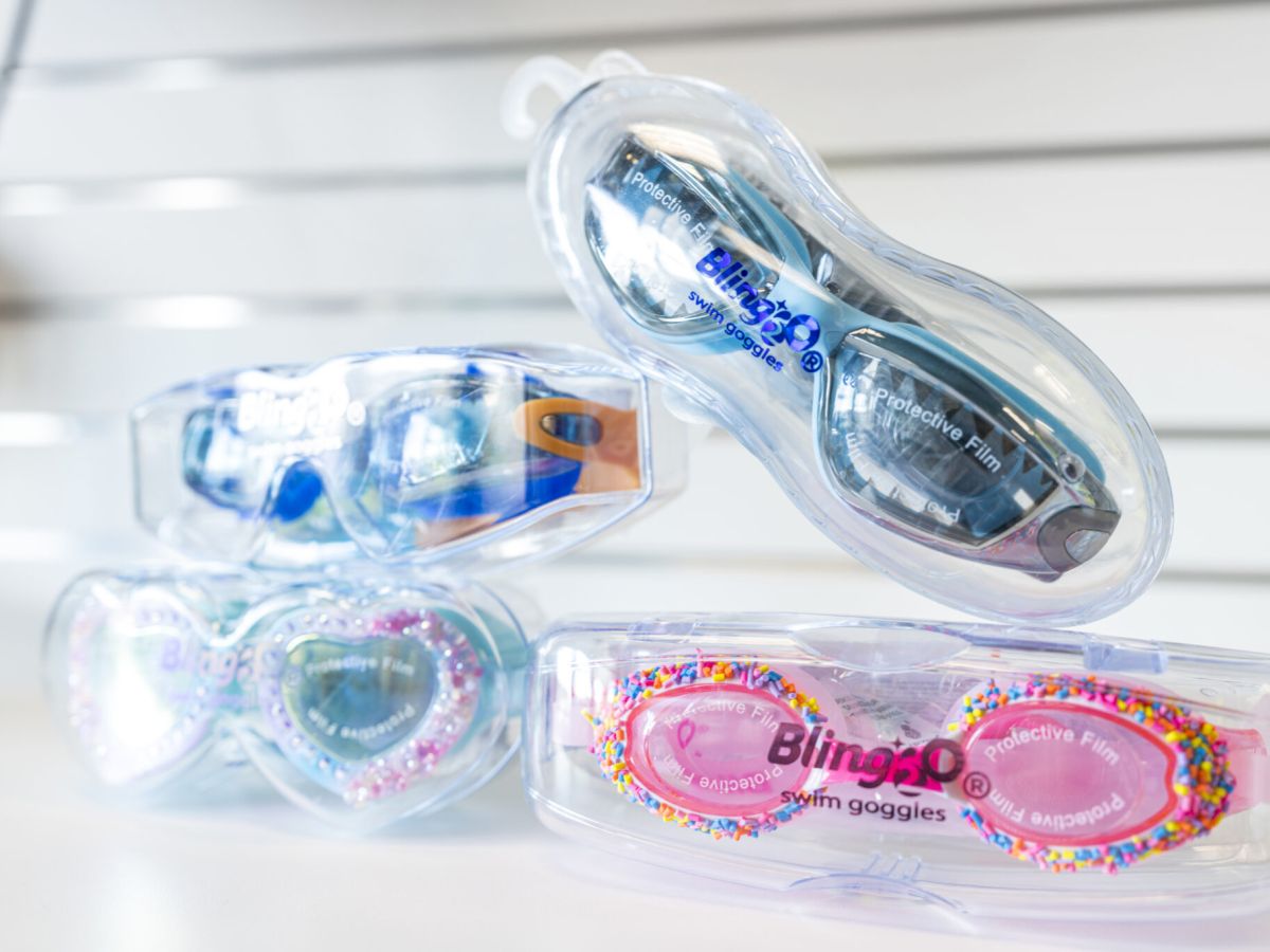 A display of colorful, clear protective eyewear in packaging, including blue, pink, and glittery designs, with goggles and case shapes, neatly arranged.