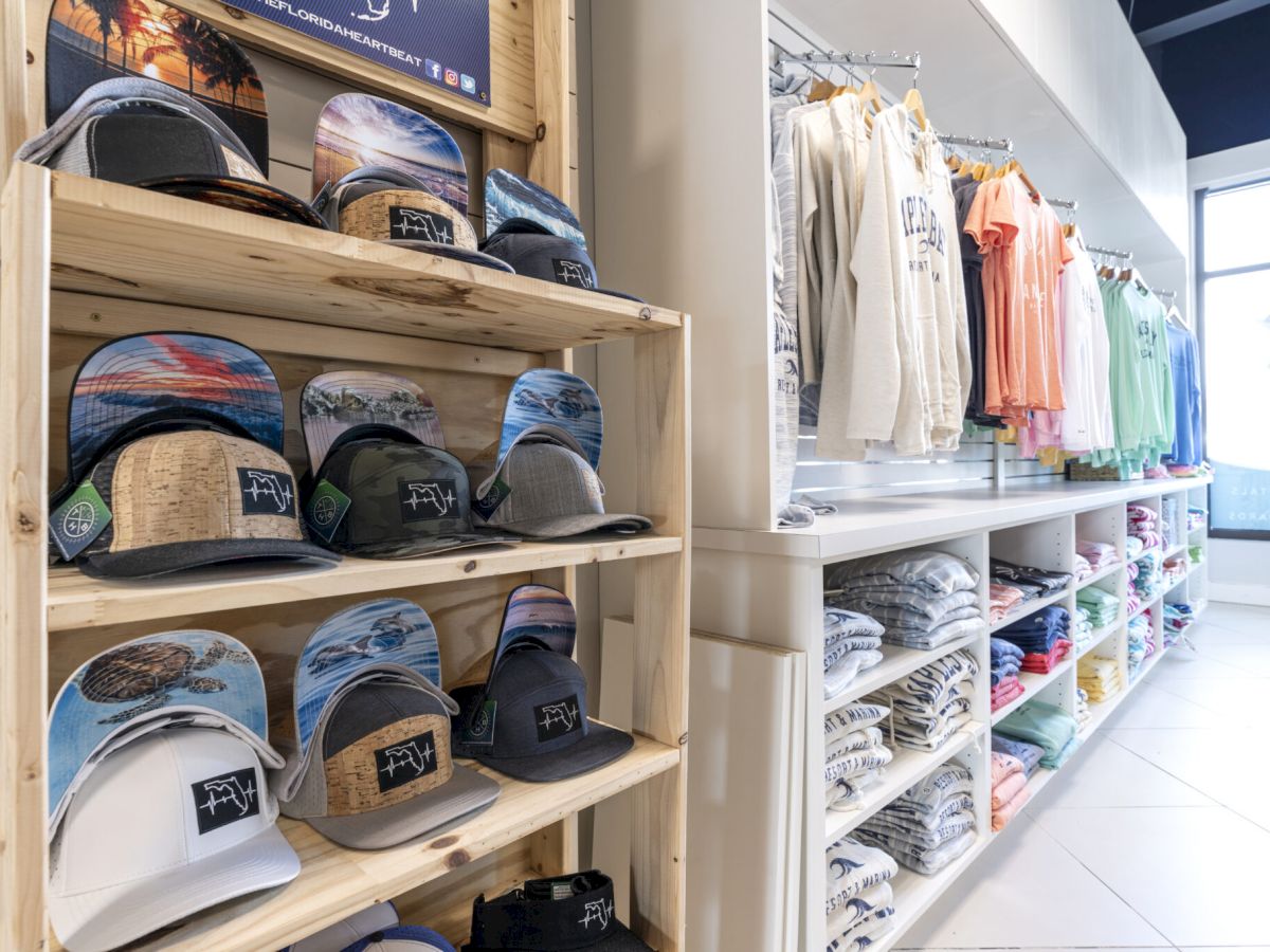 A store shelf displays hats with surf designs on the left, and neatly folded clothes on racks and shelves to the right, under bright interior lighting.
