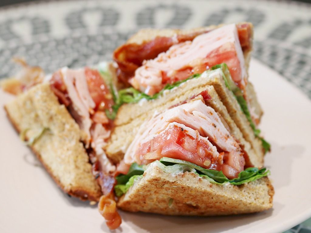 A club-style sandwich with turkey, bacon, lettuce, and tomato on toasted bread, cut into triangles on a plate.