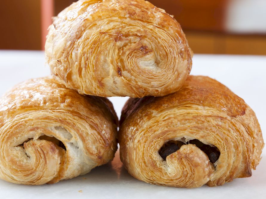 Fresh, flaky croissants stacked on a white surface, golden-brown and buttery, perfect for breakfast.