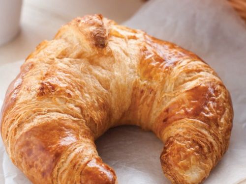 A golden, flaky croissant resting on a white napkin, buttery layers invitingly curled into a crescent.