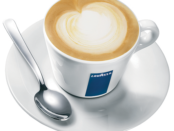 A frothy latte art coffee sits in a white cup on a saucer with a spoon, ready for a cozy break.